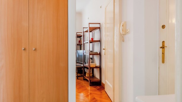 A hallway with wooden flooring, a white door with a brass handle, and a bookshelf with various items. - Cozy Studio in the Center of Zagreb (Zagreb)