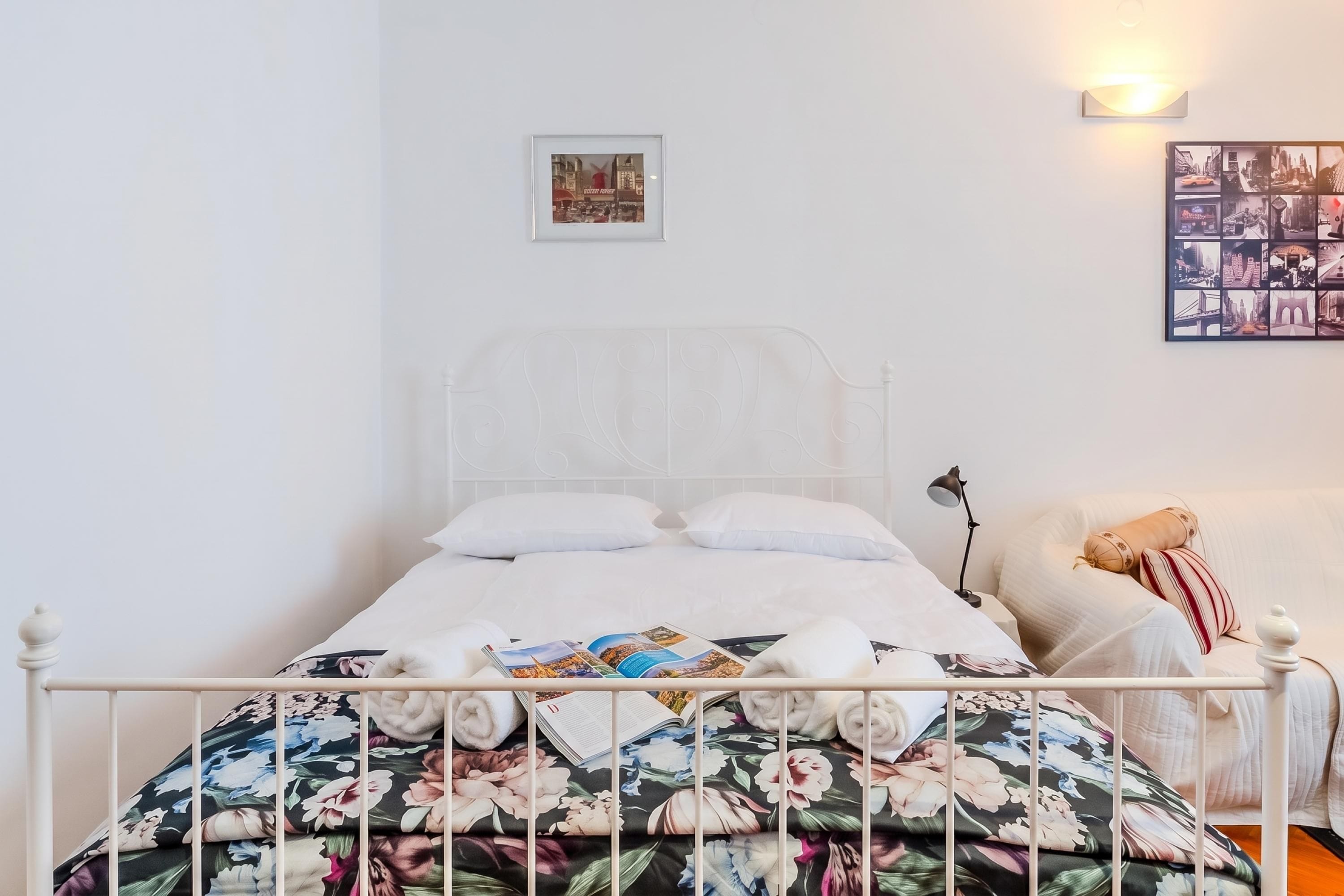 A bed with a floral bedspread, a white headboard, and a wall-mounted picture.