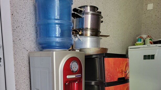 A compact kitchen with a water dispenser, a large blue water container, a stainless steel pot, and a red refrigerator. - Gabala Garden Hostel (Gabala)