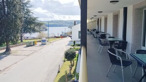 A balcony with outdoor seating overlooking a lake and mountains. - Hotel Villajardin (Portomarin)
