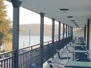 A covered outdoor seating area with tables and chairs, overlooking a body of water and hills. - Hotel Villajardin (Portomarin)