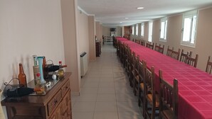 A long dining table with chairs, a wooden cabinet with bottles, and a radiator on the wall. - Hotel Villajardin (Portomarin)