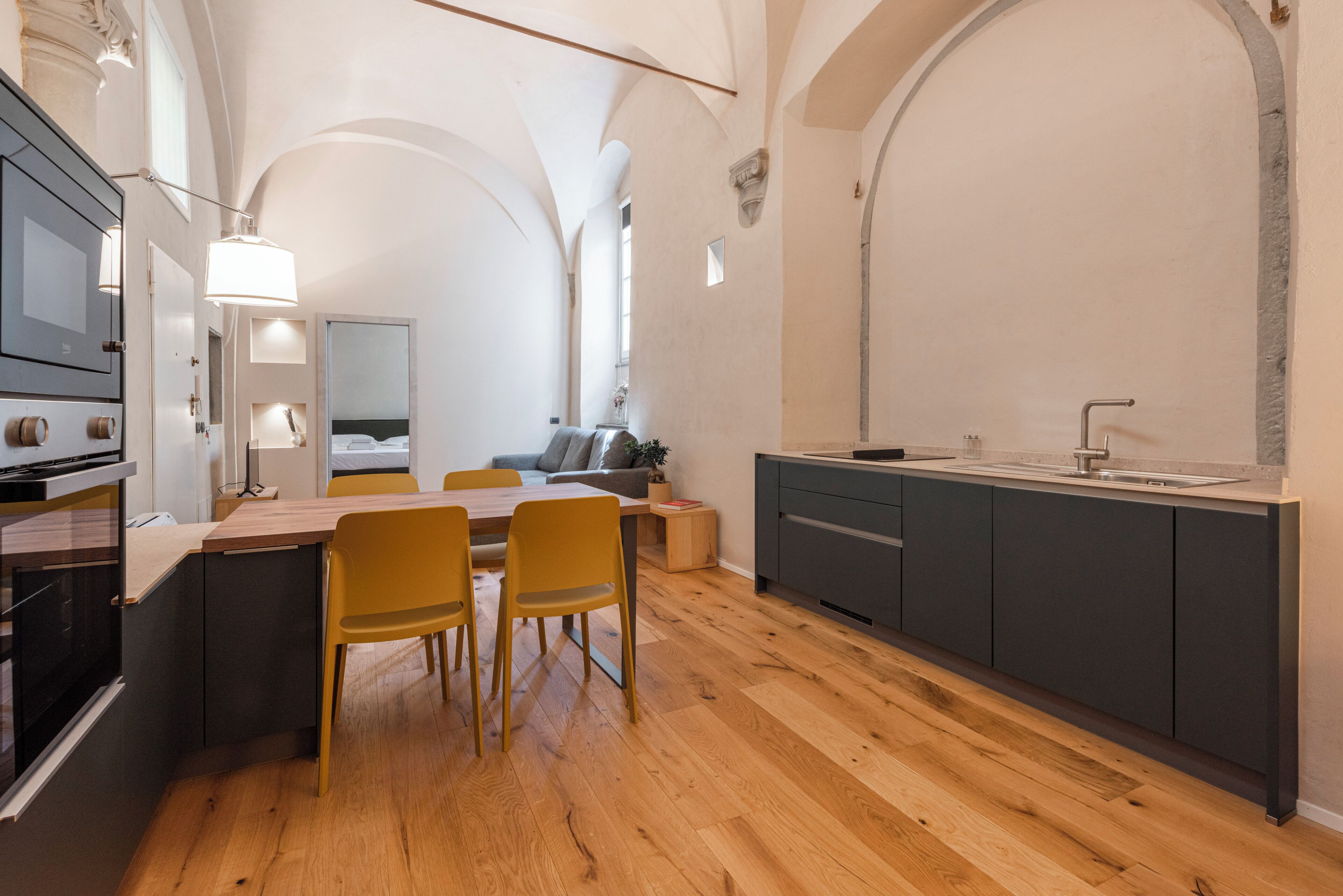 Une cuisine moderne avec un plancher en bois, un coin repas avec des chaises jaunes et un four encastré.