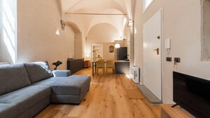 A modern living room with a grey sectional sofa, wooden flooring, a flat-screen TV, and a dining area with chairs. - Ramaglianti Hidden Gem by Mmega (Florence)