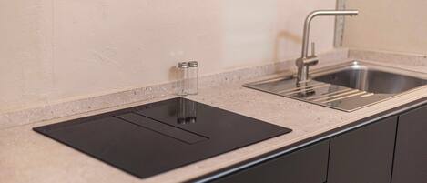 A kitchen with a black induction cooktop, a stainless steel sink, and a single faucet.