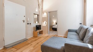 A modern living room with a grey sofa, wooden flooring, a television, and a door leading to another room. - Ramaglianti Hidden Gem by Mmega (Florence)