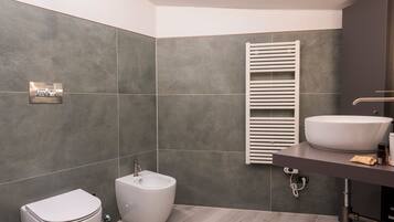 A modern bathroom with grey tiles, a bidet, a toilet, a white sink, and a towel rack.