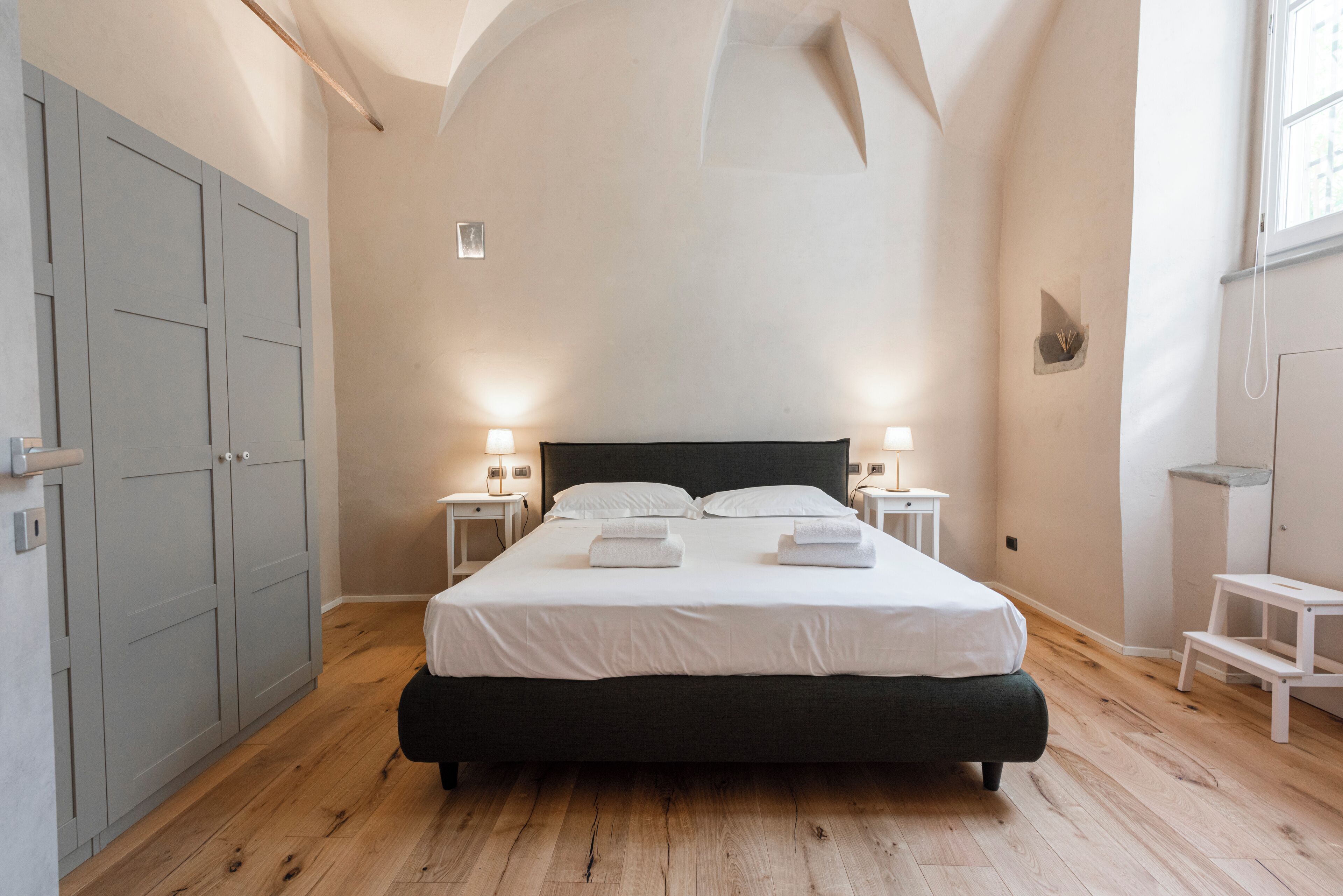Un dormitorio con una cama grande, dos mesitas de noche con lámparas, un armario y una ventana.