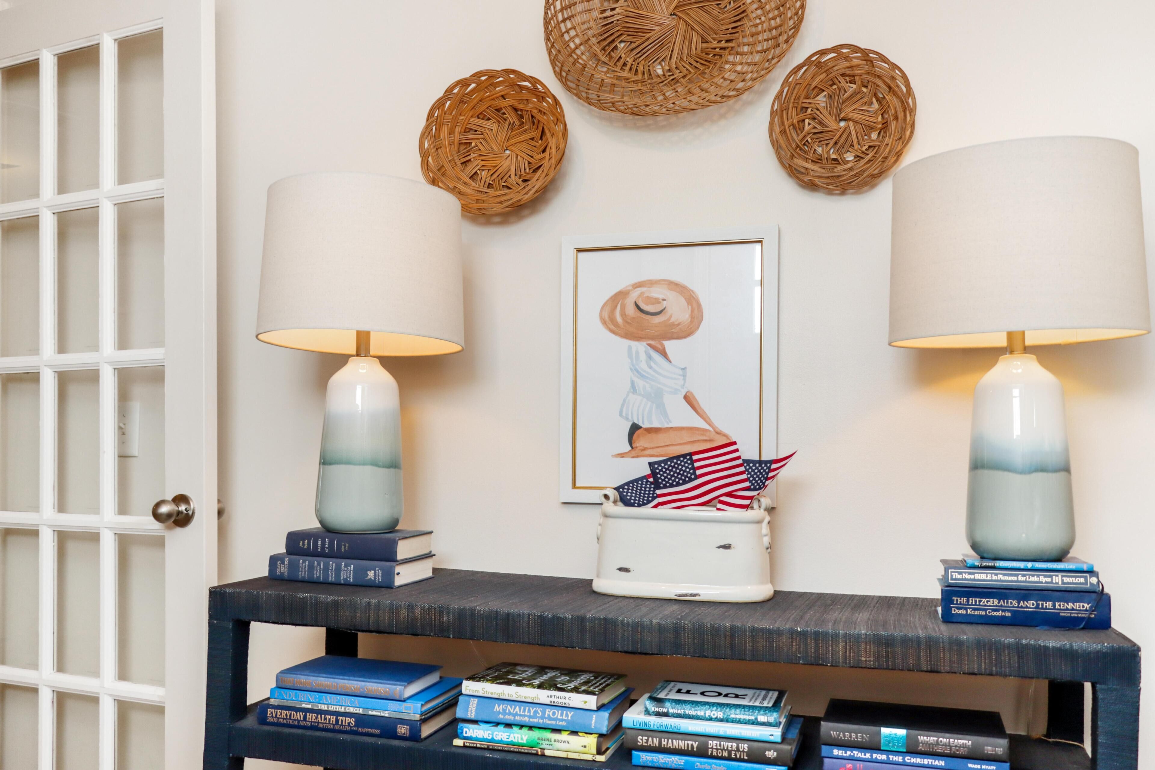 Ein Zimmer mit einer weißen Tür, einer Wand mit gewebten Körben, einem gerahmten Bild und einem Regal mit Büchern und einer Lampe.