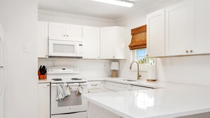A modern kitchen with white cabinetry, a built-in microwave, a stove, and a sink. - 1st Street Bungalow (Port St. Joe)