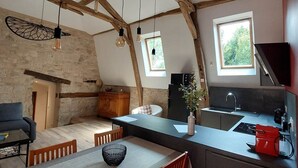 A modern kitchen with exposed wooden beams, a dining area with a table and chairs, and a stone wall. - Château de Belmont Ste Foi - a place steeped in history ! (Belmont-Sainte-Foi)