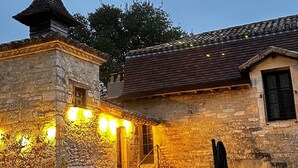 A stone building with a tiled roof, a small tower, and a staircase leading to the entrance. There are potted plants and an umbrella in the foreground. - Château de Belmont Ste Foi - a place steeped in history ! (Belmont-Sainte-Foi)