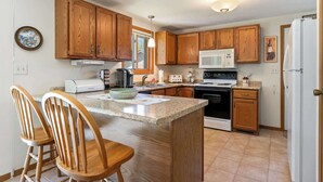 Et køkken med træskabe, en mikrobølgeovn, komfur, køleskab og et spiseområde med stole.
