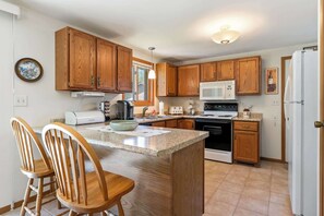 A kitchen with wooden cabinets, a microwave, a stove, a refrigerator, and a dining area with chairs.