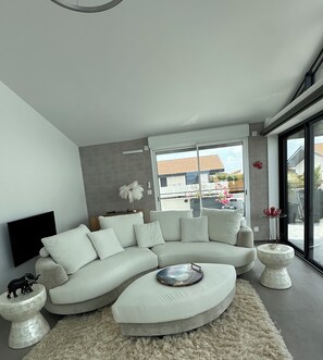 A modern living room with a sectional sofa, a flat-screen TV, and a large window offering a view of the outside.