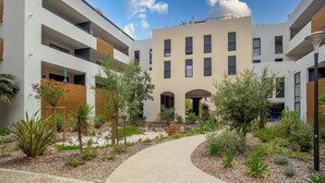 A modern multi-story building with a central courtyard, featuring a pathway and various plants.