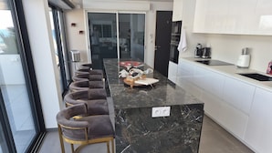 A modern kitchen with a marble island, bar stools, and a large window.