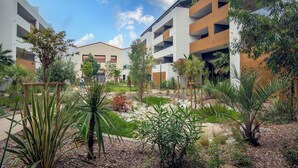 A modern residential complex with multiple-story buildings, a landscaped courtyard with various plants, and a clear sky.