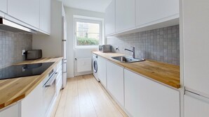 Una cucina moderna con mobili bianchi, un piano di lavoro in legno, una lavatrice integrata e una finestra che permette l'illuminazione naturale.