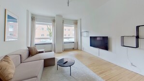 Un soggiorno moderno con un divano, un tavolino, una TV a schermo piatto montata a parete e ampie finestre con tende.