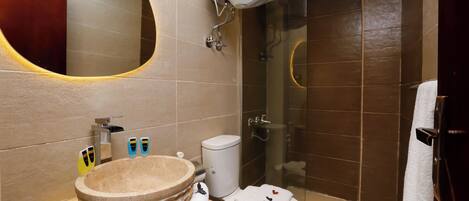 A bathroom with a round sink, a toilet, a shower, and a mirror.