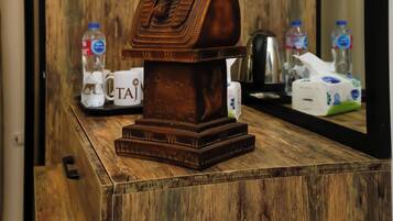 Un mobiletto in legno con un busto decorativo, un telecomando, una scatola di fazzoletti e una bottiglia d'acqua.
