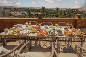 A table set with various breakfast items and a view of palm trees and hills. - Taj pyramids view inn (Giza)
