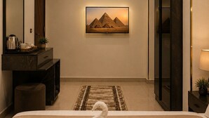 A hotel room with a bed, a desk, a mirror, a wall-mounted TV, and a door. - Taj pyramids view inn (Giza)