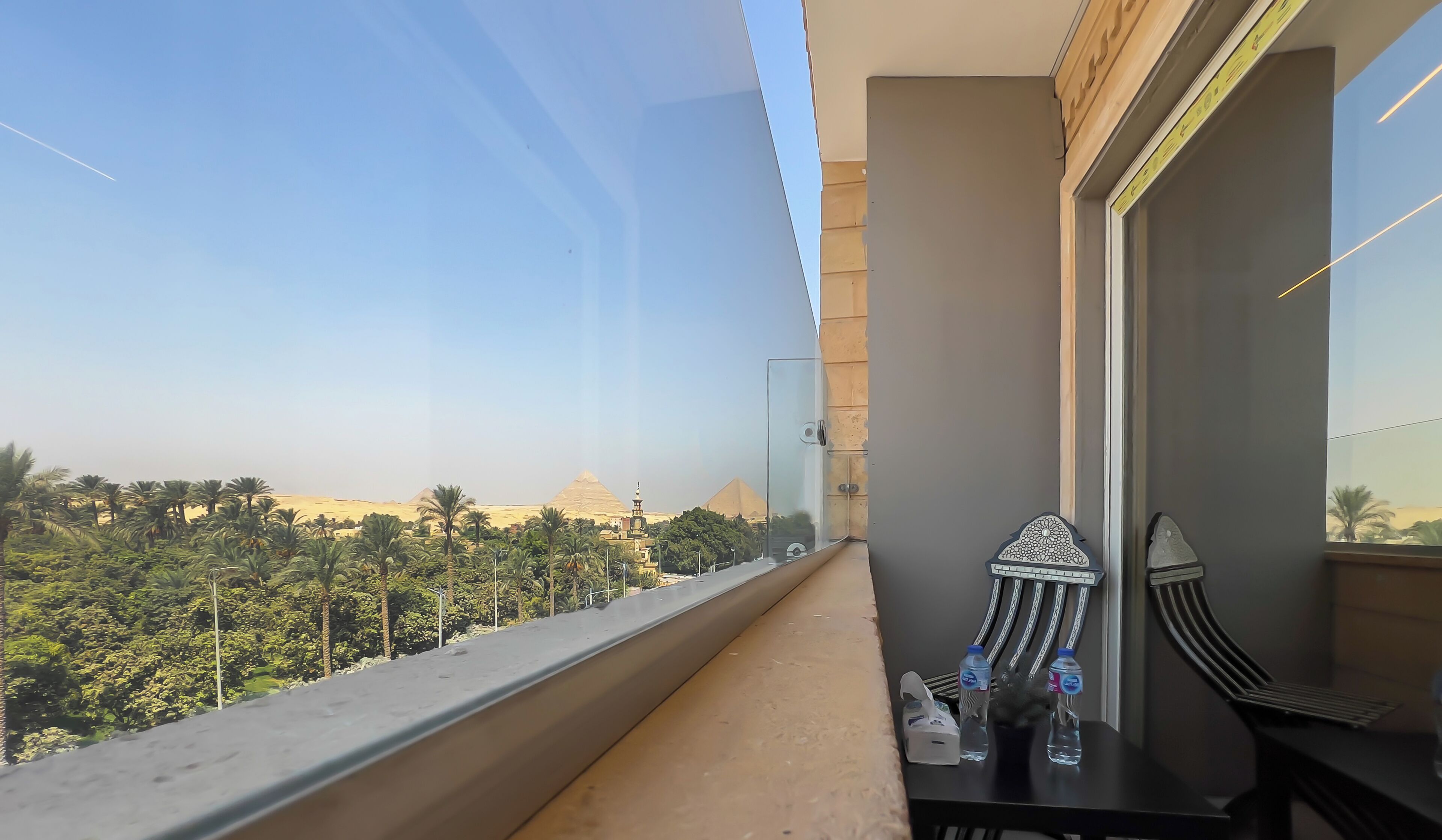 A balcony with a view of the pyramids and palm trees.