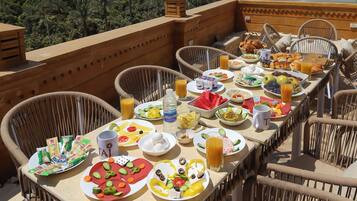 A breakfast table set with various dishes and drinks, overlooking a scenic view of pyramids and palm trees.