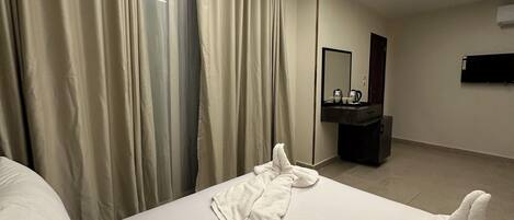 Een hotelkamer met een groot bed, een nachtkastje, een spiegel en een raam met gordijnen.