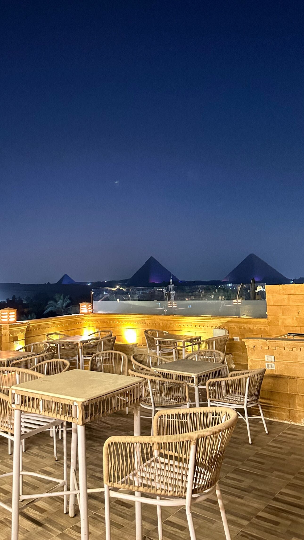 An outdoor dining area with tables and chairs, a view of a mountain range, and a clear night sky.