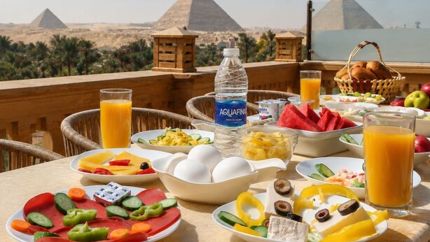 A breakfast table with various dishes, a bottle of water, and a view of pyramids. - Taj pyramids view inn (Giza)