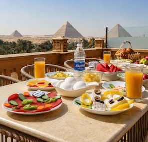 A breakfast table with various dishes, a bottle of water, and a view of pyramids. - Taj pyramids view inn (Giza)