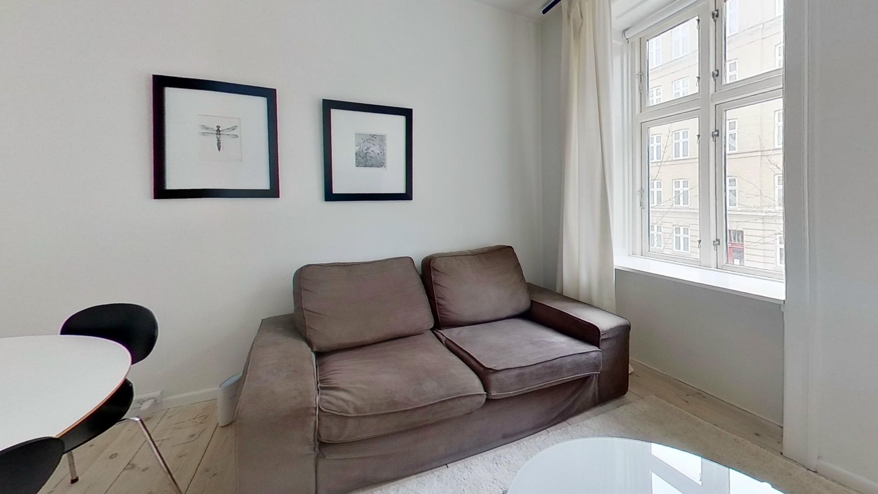 A living room with a brown sofa, a white table, and two framed pictures on the wall.