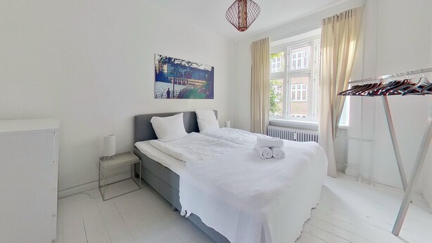 A neatly arranged bedroom with a bed, a side table, a window with curtains, and a wall-mounted picture. - Cool 1-bed Apartment in Rhus (Aarhus)