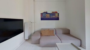 A modern living room with a sectional sofa, a flat-screen TV, and a cityscape painting on the wall. - Cool 1-bed Apartment in Rhus (Aarhus)