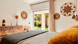 Un dormitorio con cama, cómoda, silla y vista a un jardín a través de una puerta corrediza.