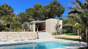 Una casa moderna con piscina, mobiliario exterior y un muro de piedra.