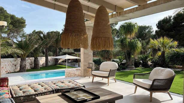 Un patio al aire libre con piscina, mobiliario de mimbre y lámparas colgantes.