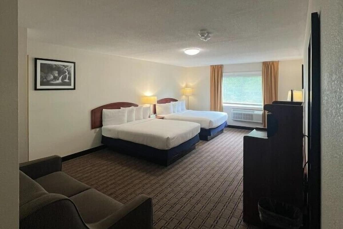 A hotel room with two beds, a sofa, a desk, a TV, and a picture on the wall.