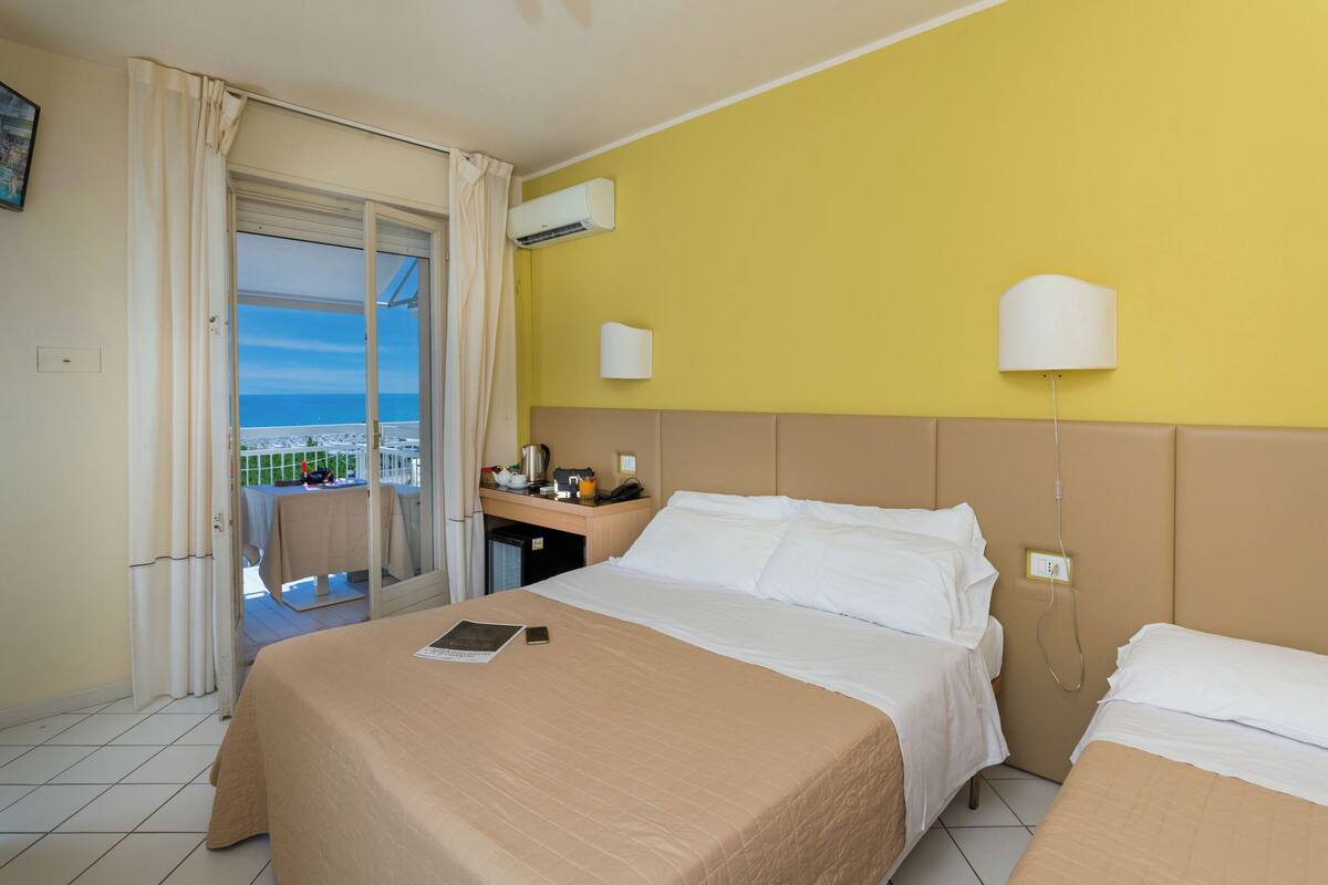 A hotel room with a bed, a desk, a chair, and a view of the sea.