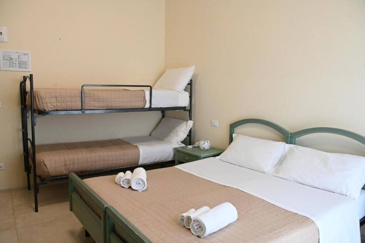 A hotel room with a bunk bed, a single bed, and a nightstand with a lamp.