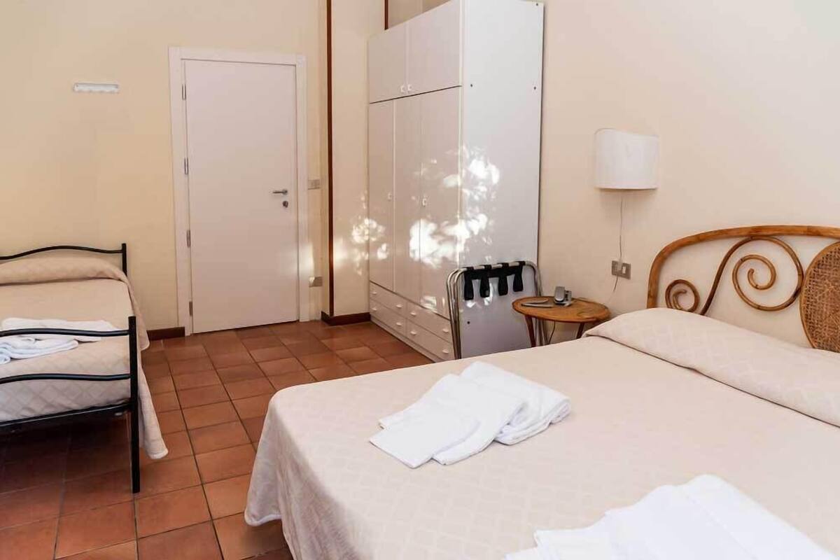 A hotel room with a bed, a wardrobe, a small table with a lamp, and a door.