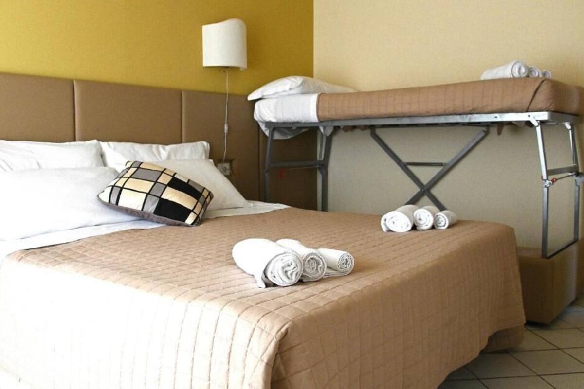 A hotel room with a bed, a bunk bed, and a bedside table with rolled towels.