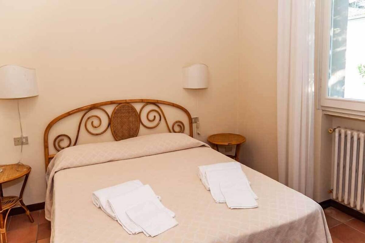 A neatly made bed with two towels, a small round table, and a wall-mounted lamp.