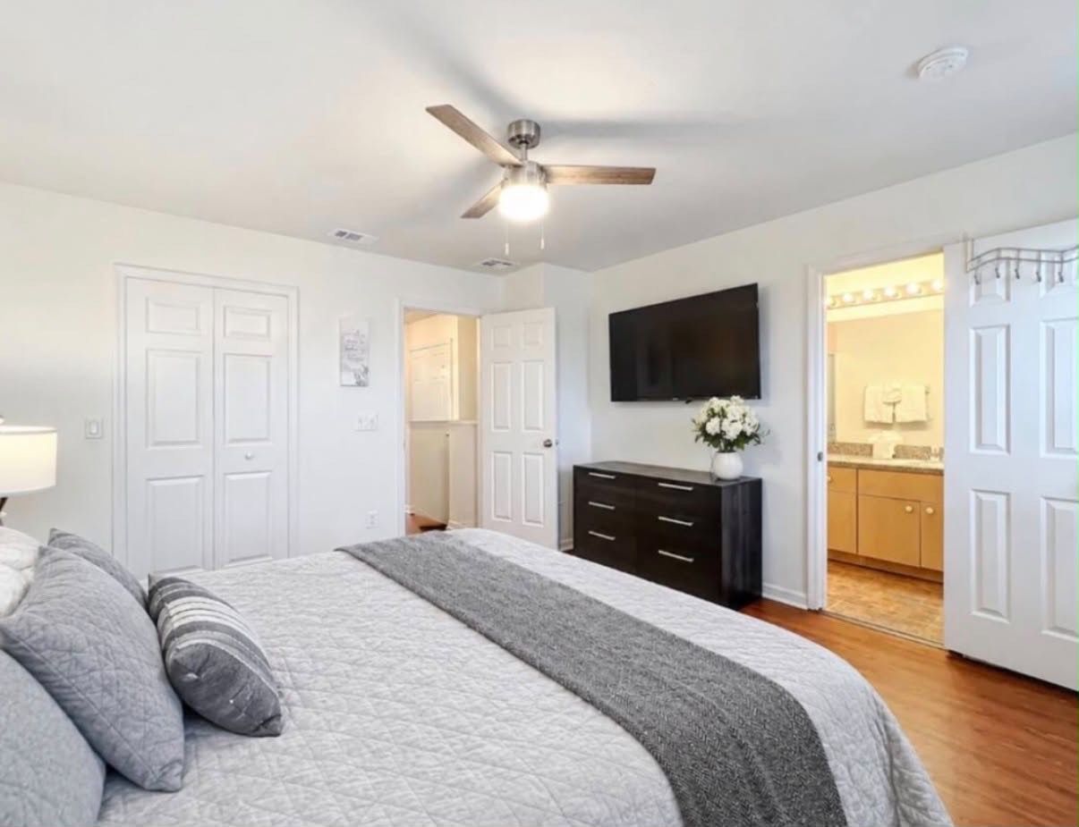 Une chambre à coucher comprenant un lit, une commode, un ventilateur de plafond et un téléviseur.