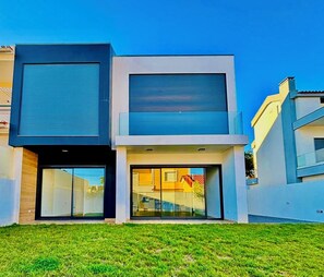 A modern two-story house with large sliding glass doors, a flat roof, and a well-maintained lawn.