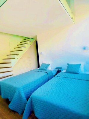 A room with two beds, a small table, and a staircase.