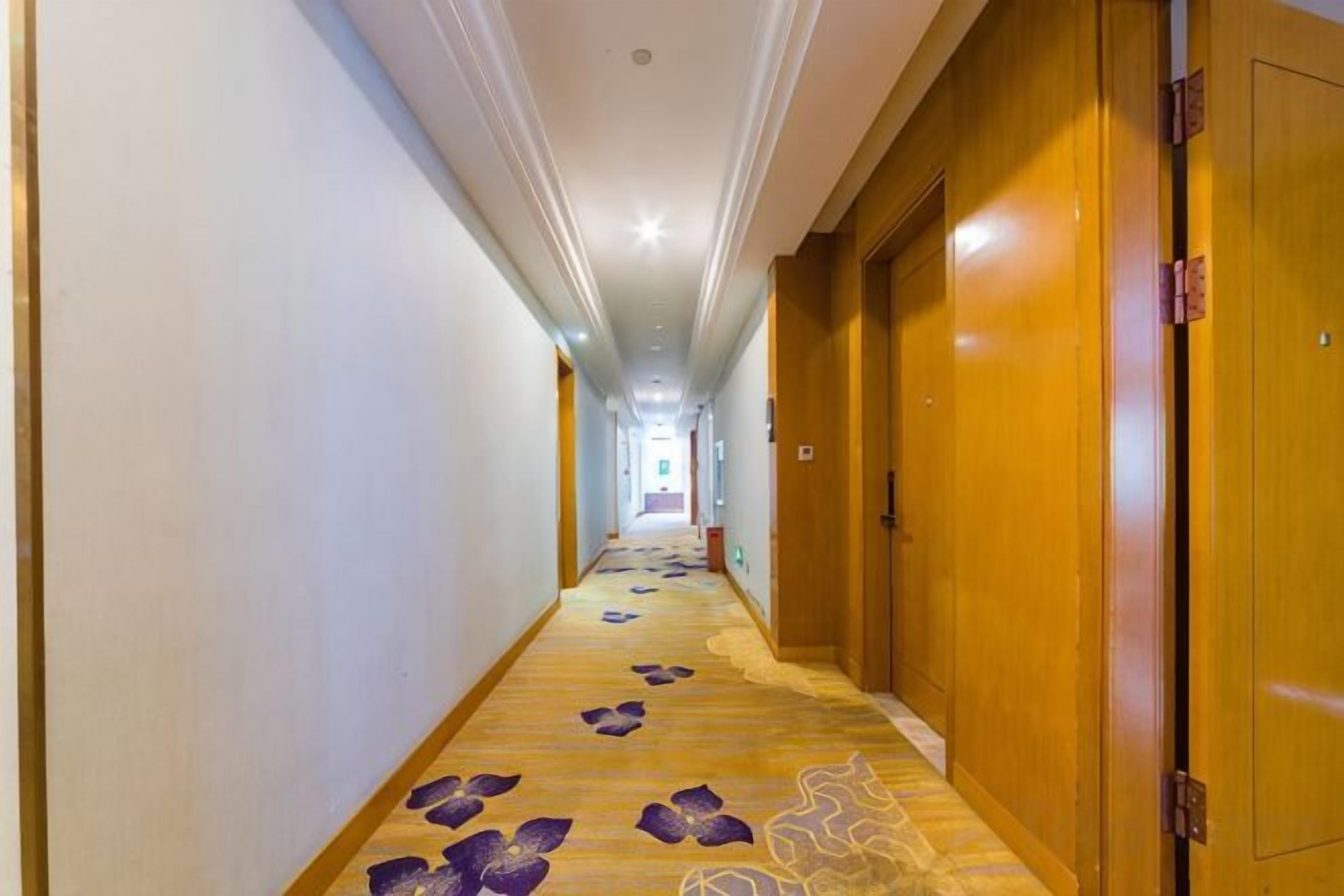 Un pasillo de hotel con puertas de madera, suelo alfombrado y pared de color claro.